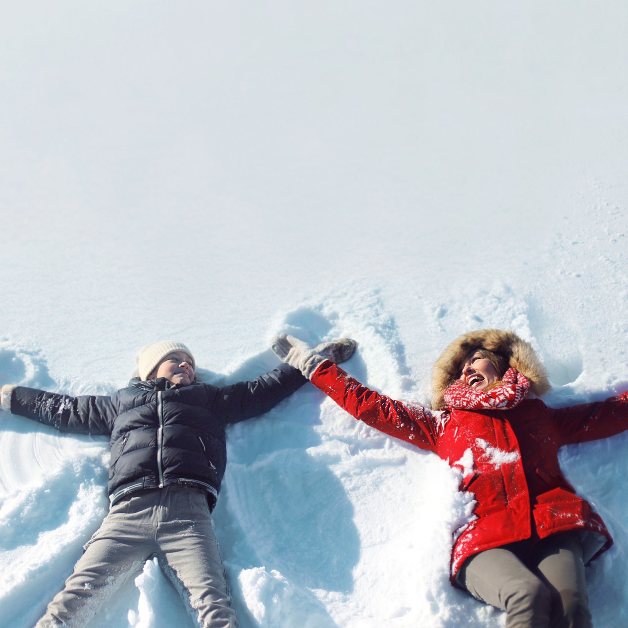 Happy mother, son playing having fun lying in snow winter