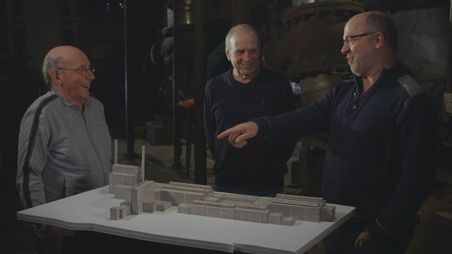 Des anciens employés de la CIP devant une maquette de leur usine réalisée en papier journal. Photo: Collaboration spéciale/ONF