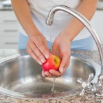 Mid section of hands washing apple at washbasin