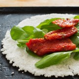 Casabe (bammy, beiju, bob, biju) - flatbread made from cassava (tapioca) with sun-dried tomatoes and rucola (arugula) on pan. Selective focus