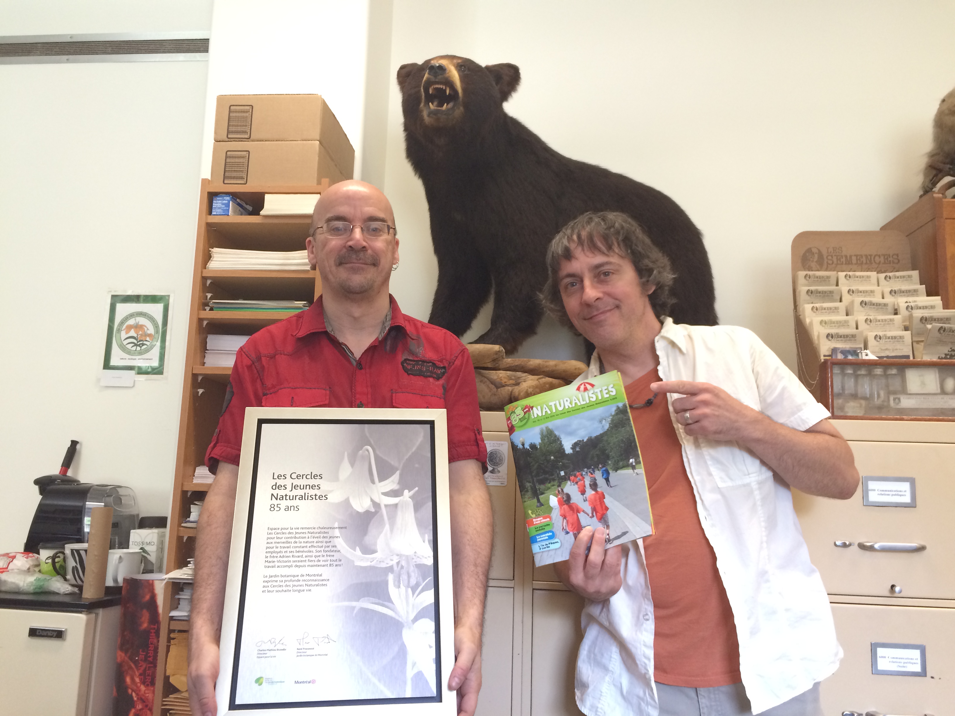 André St-Arnaud et André Cyr posent devant une des mascottes des CJN depuis 1984, l'ours Bruno le Grognon.