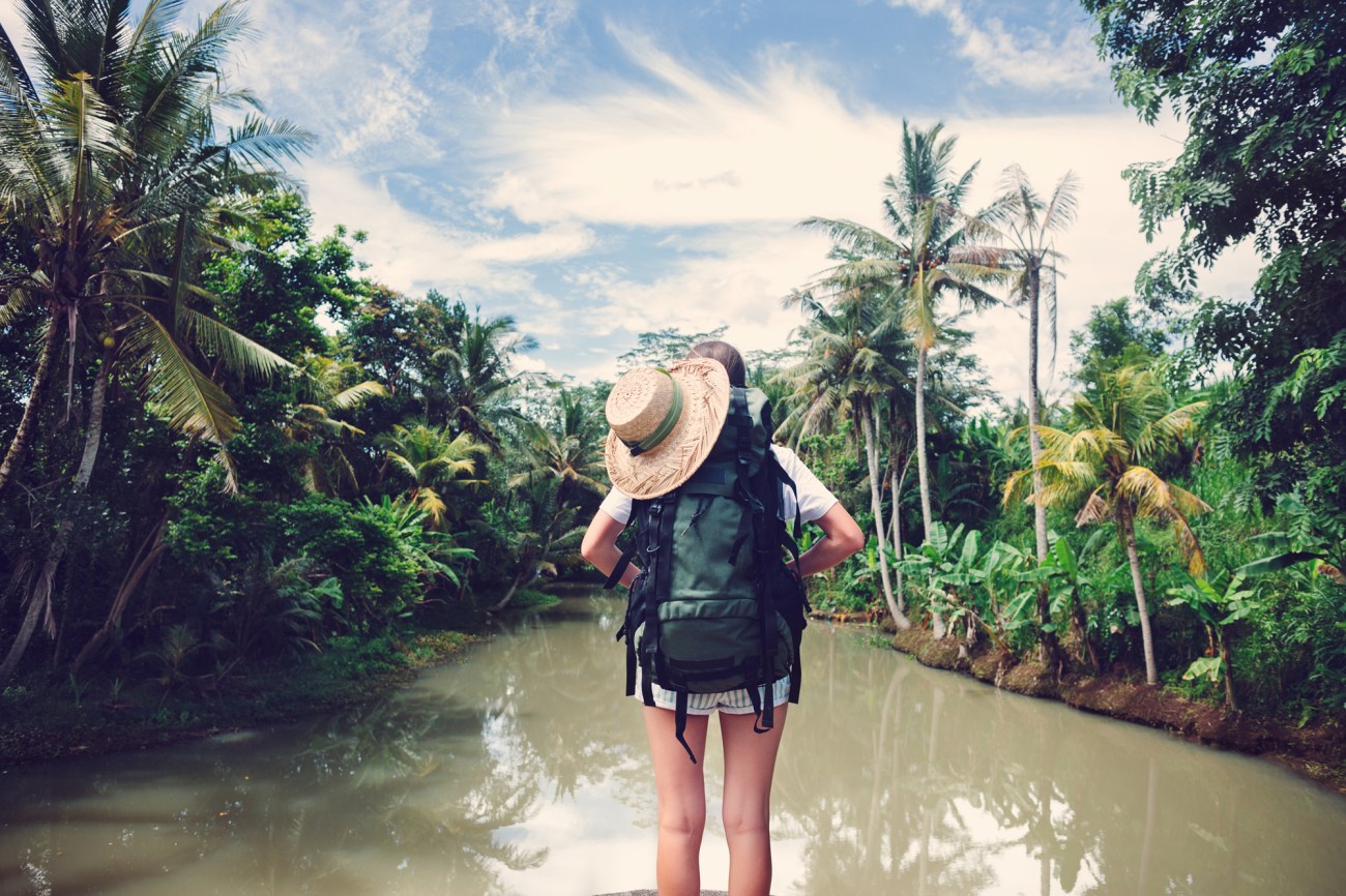 Woman traveler with backpack standing near tropical river (intentional vintage color)