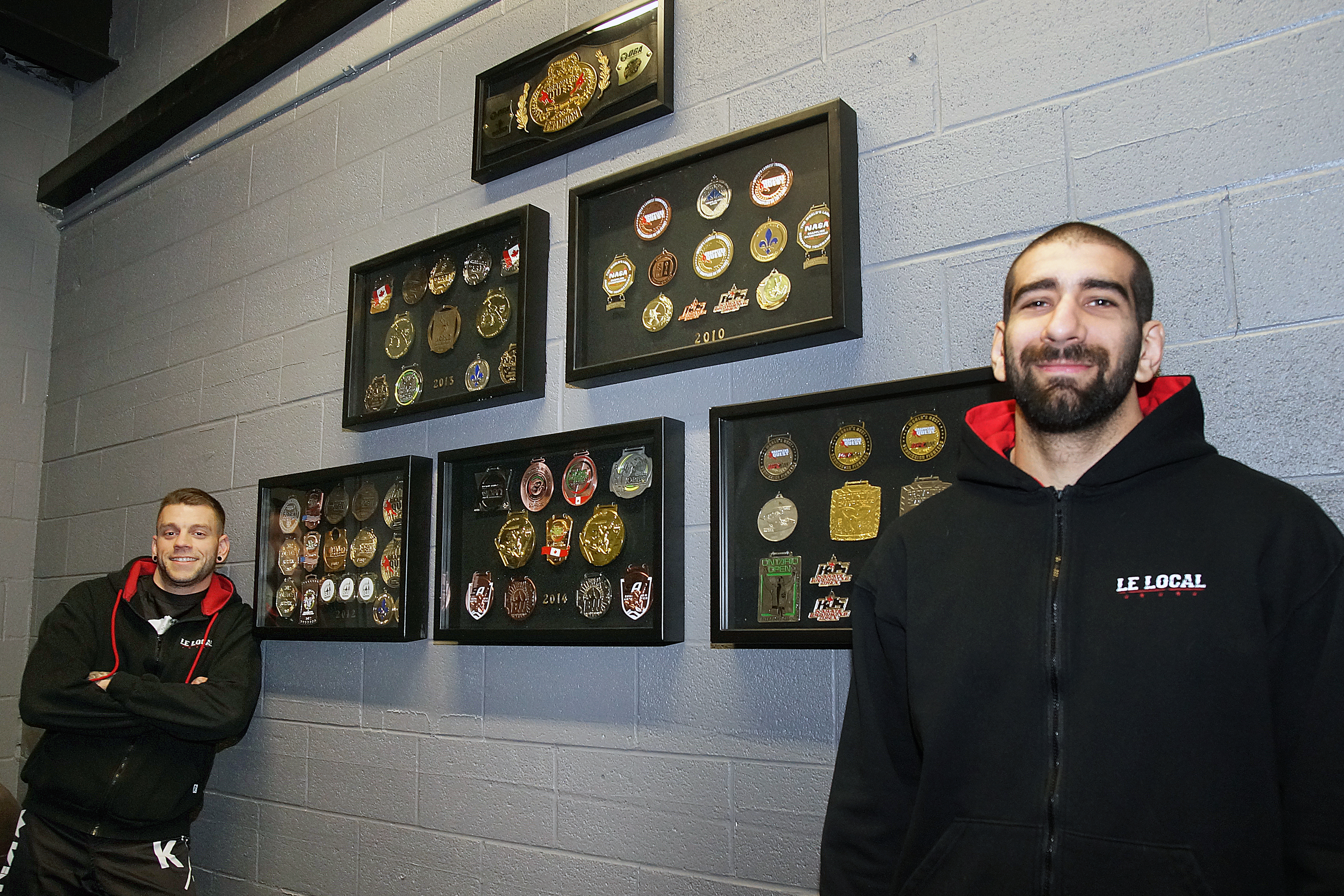Keven Sénécal (gauche) et Karl Fagnant, copriopriétaires du Gym Le Local, à Montréal-Est, posent devant leur tableaux de médailles le 29 mars 2017.
