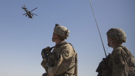 Des soldats américains en Afghanistan regardent un hélicoptère d’attaque AH-64 Apache.