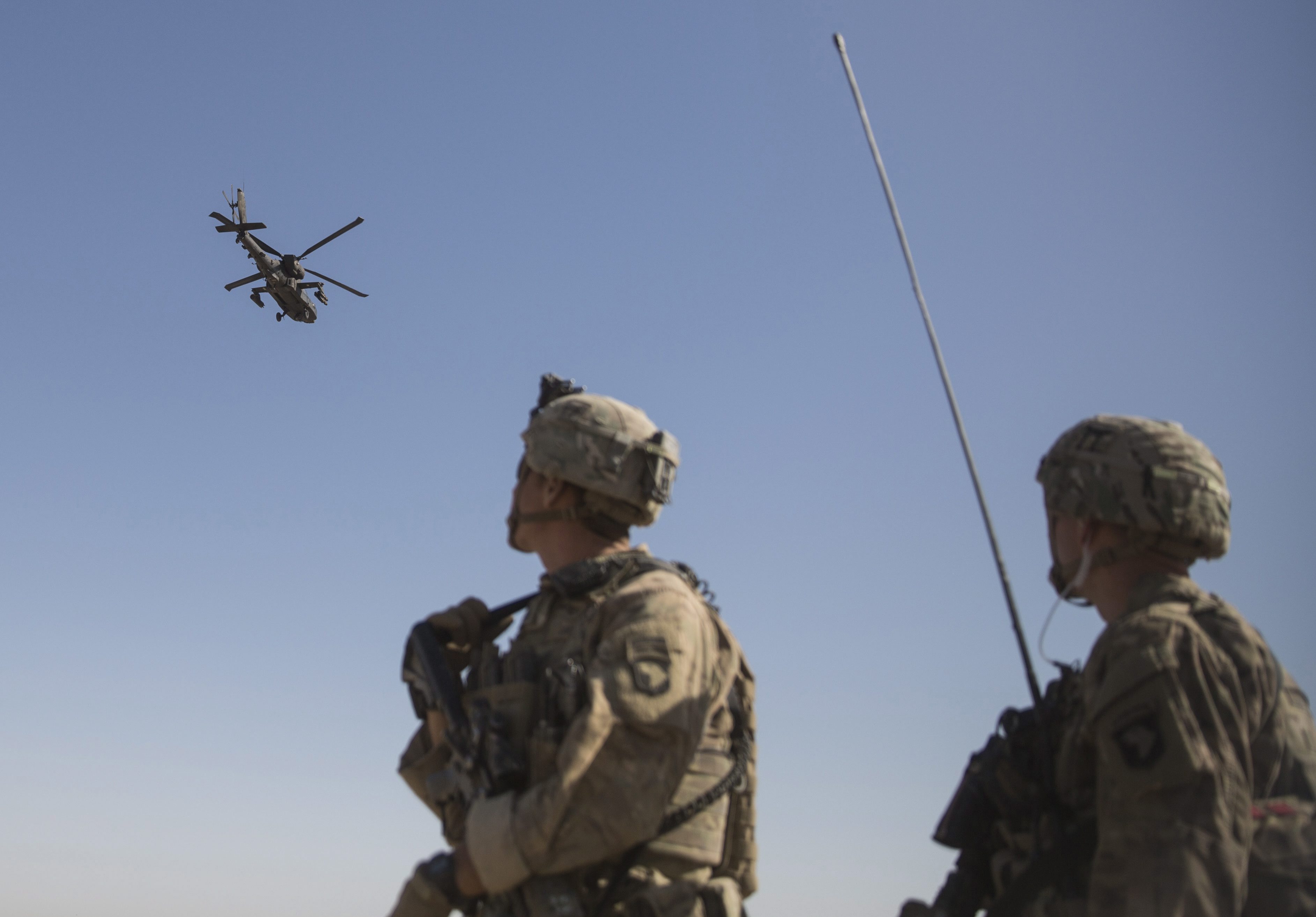 Des soldats américains en Afghanistan regardent un hélicoptère d’attaque AH-64 Apache.