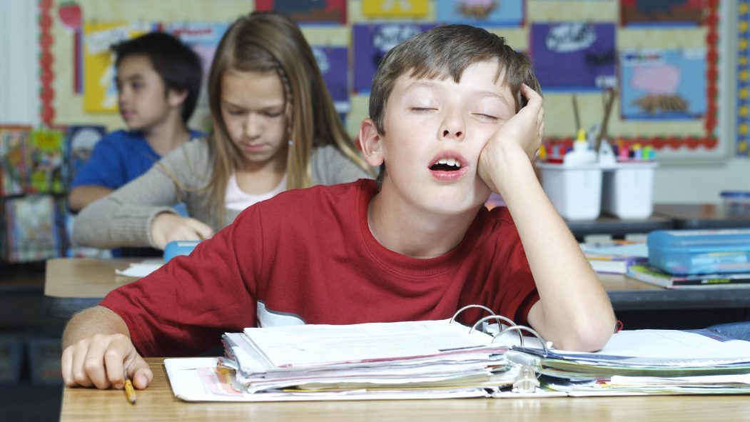 Un enfant dort en classe, le coude appuyé sur son pupitre.