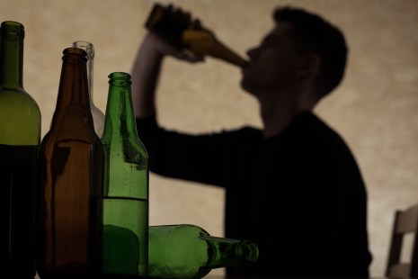 bouteilles vides et silhouette d'un jeune homme qui consomme de l'alcool