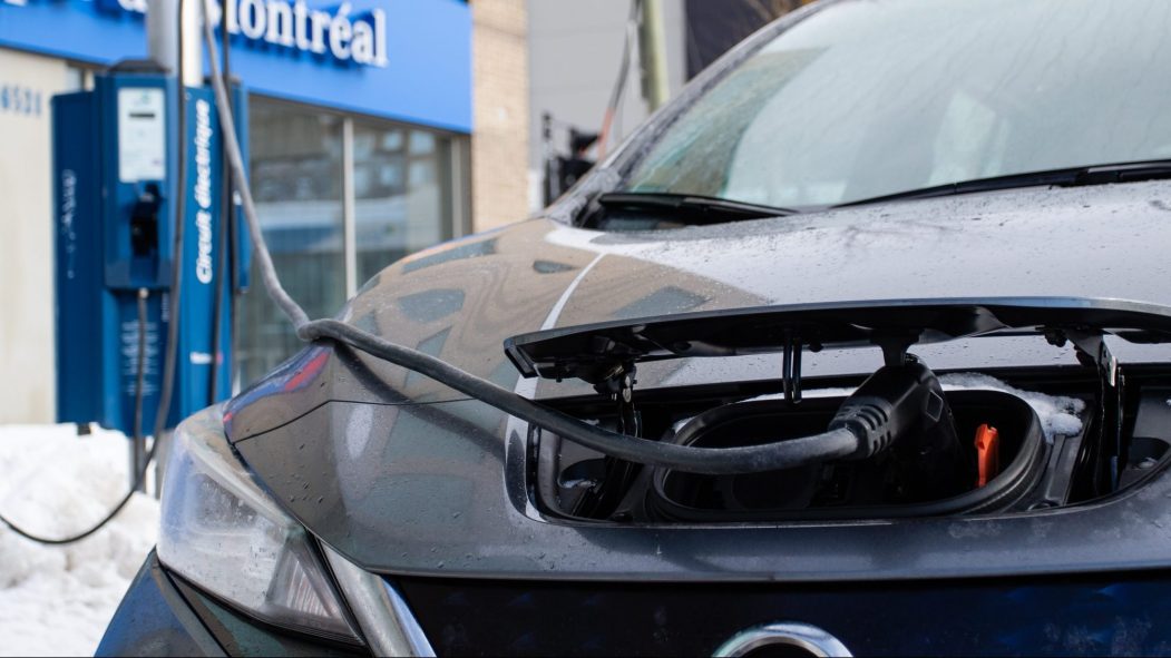 Une voiture branchée sur une borne de recharge de véhicules électriques devant une succursale de la Banque de Montréal.