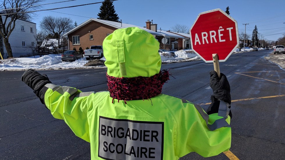 Un brigadier scolaire habillé en vert tenant son panneau d'arrêt levé.