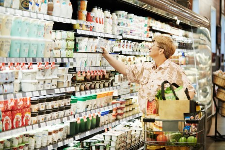 Une dame prend un yaourt sur une étagère dans un supermarché.