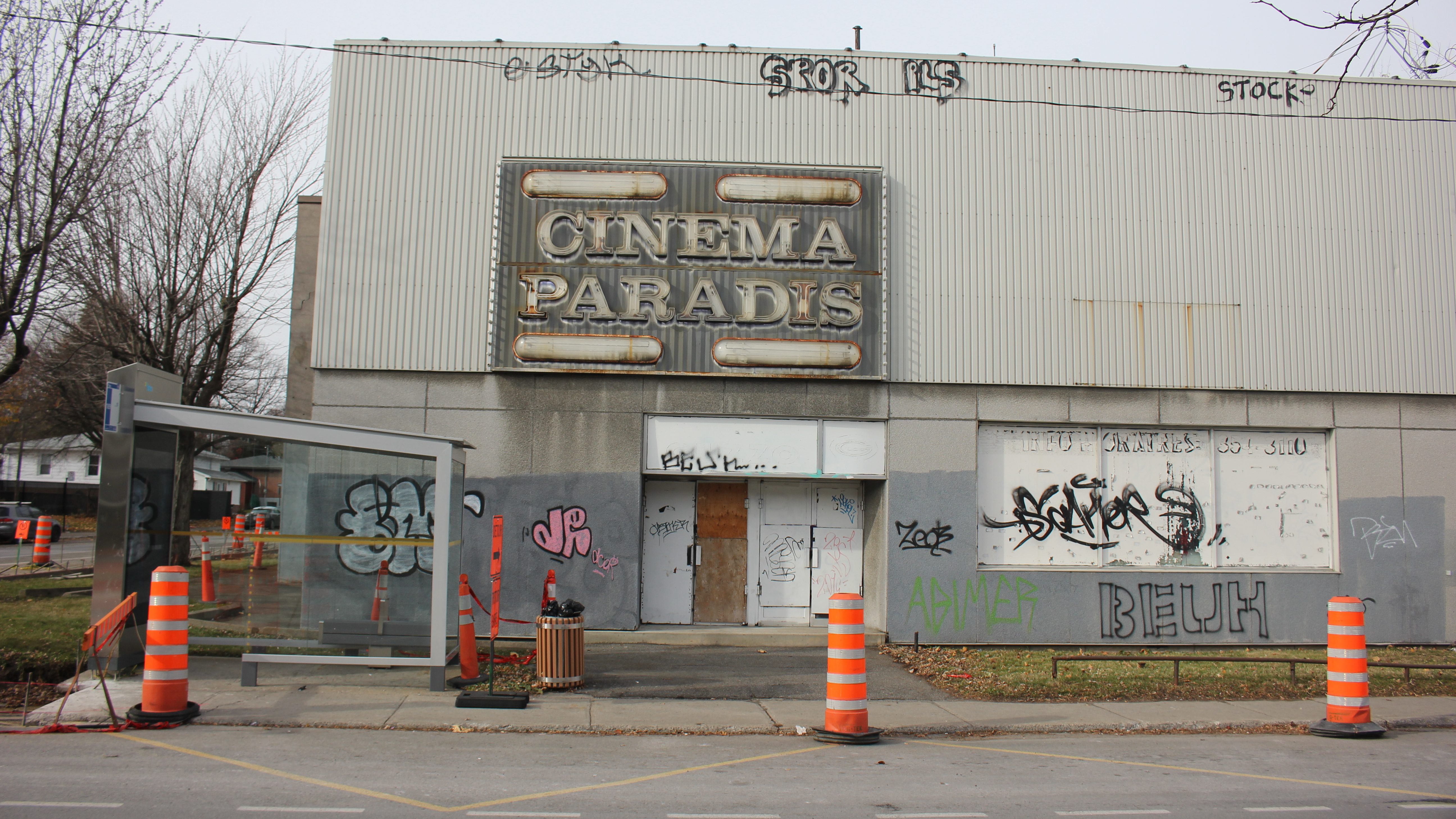 La façade du bâtiment délabré de l'ancien cinéma Paradis, montrant des portes et fenêtres barricadées et des graffitis. Des cônes oranges sont placés devant le bâtiment.