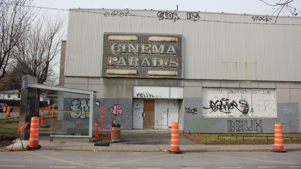 La façade du bâtiment délabré de l'ancien cinéma Paradis, montrant des portes et fenêtres barricadées et des graffitis. Des cônes oranges sont placés devant le bâtiment.