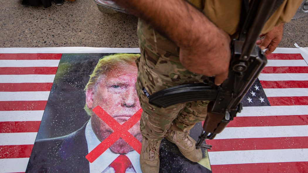 Un membre des forces irakiennes Hachd al-Chaabi marche sur un drapeau américain affichant une photo de Donald Trump avec un grand X.