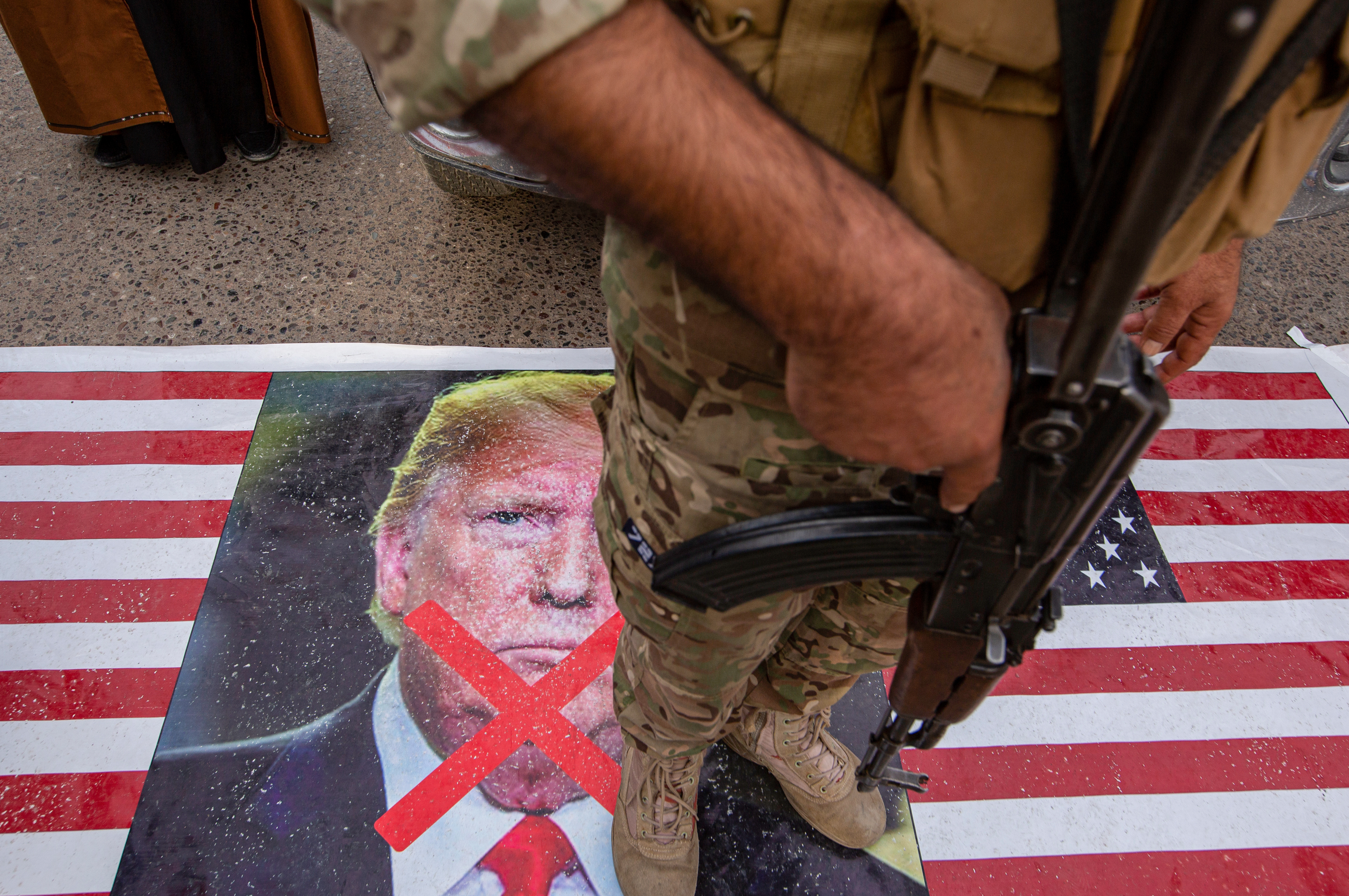 Un membre des forces irakiennes Hachd al-Chaabi marche sur un drapeau américain affichant une photo de Donald Trump avec un grand X.