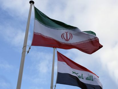 Les drapeaux iranien et irakien flottent devant un ciel bleu partiellement ennuagé.