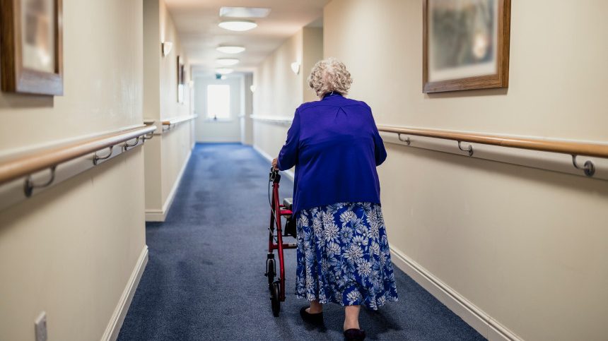 Une femme âgée se promène en marchette dans une résidence pour personnes âgées.