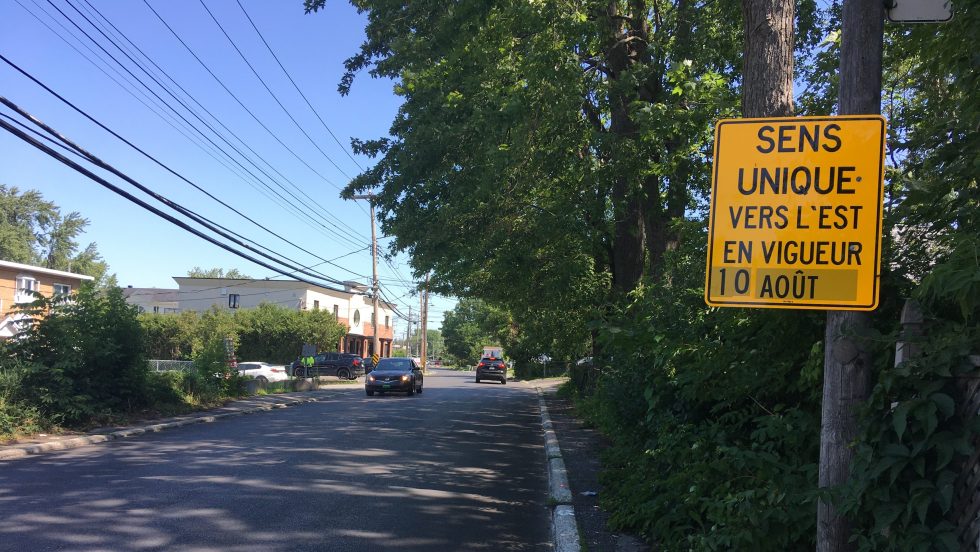 Une voiture circule vers l'ouest derrière un panneau de signalisation.
