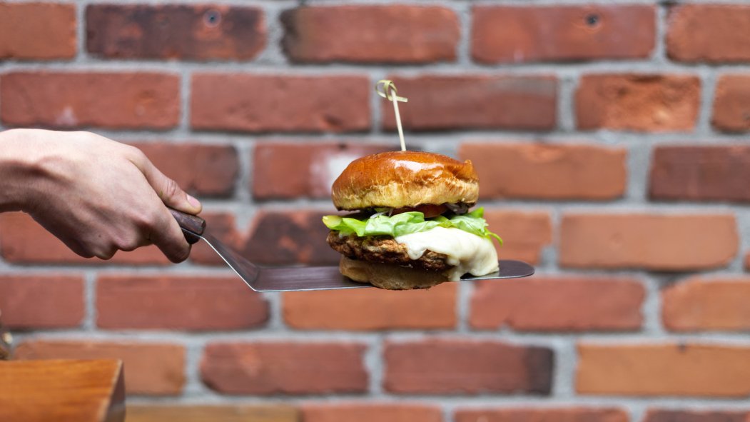 Main tenant une spatule contenant un burger