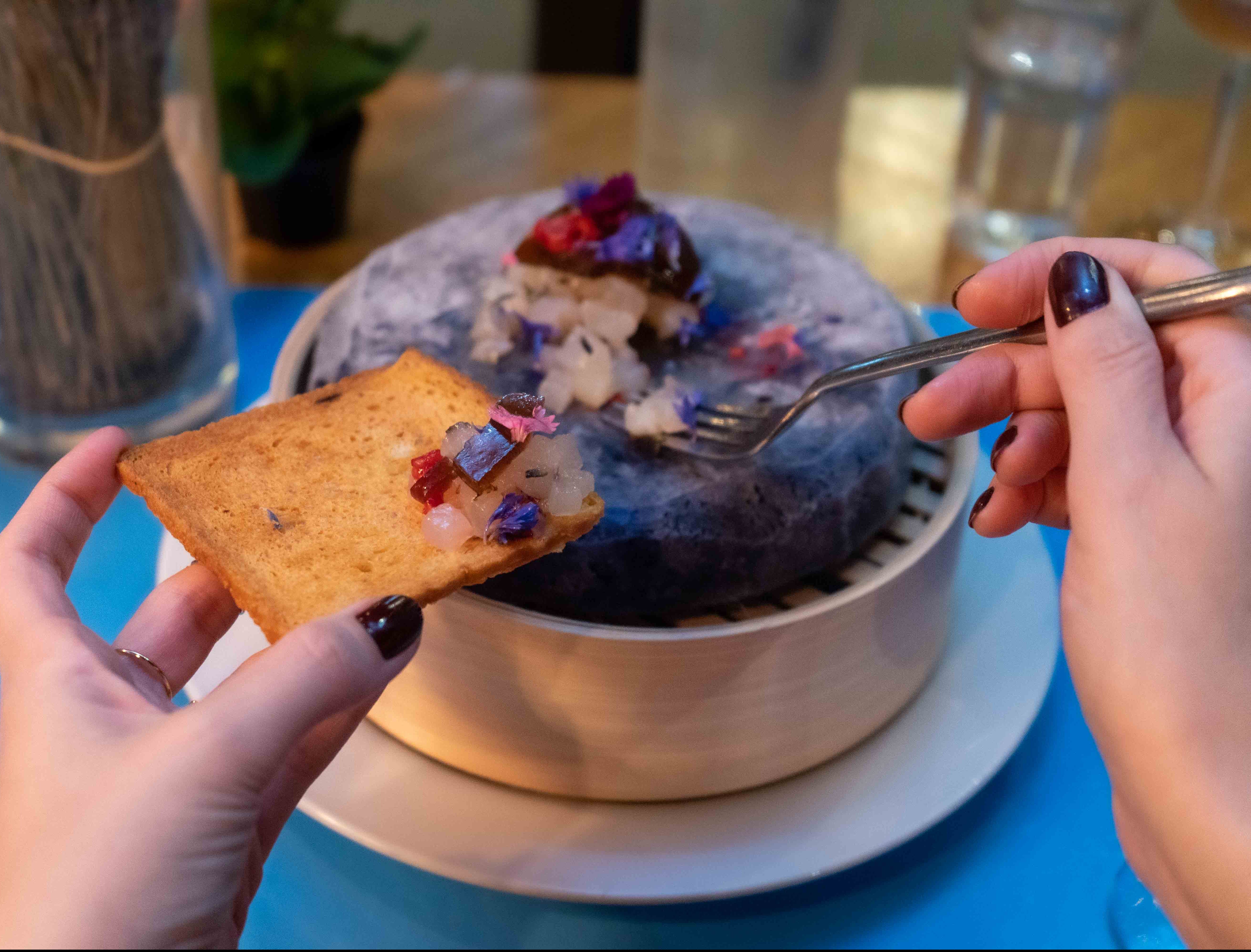 Deux mains tenant fourchette et croûton face à un plat de tartare