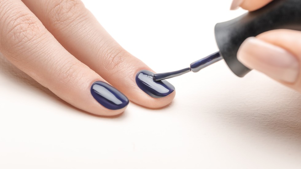 female manicurist applying navy blue nail polish on fingernail of woman on white background