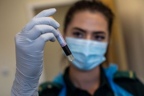 Une chercheuse portant un masque tient dans ses mains un flacon de sang