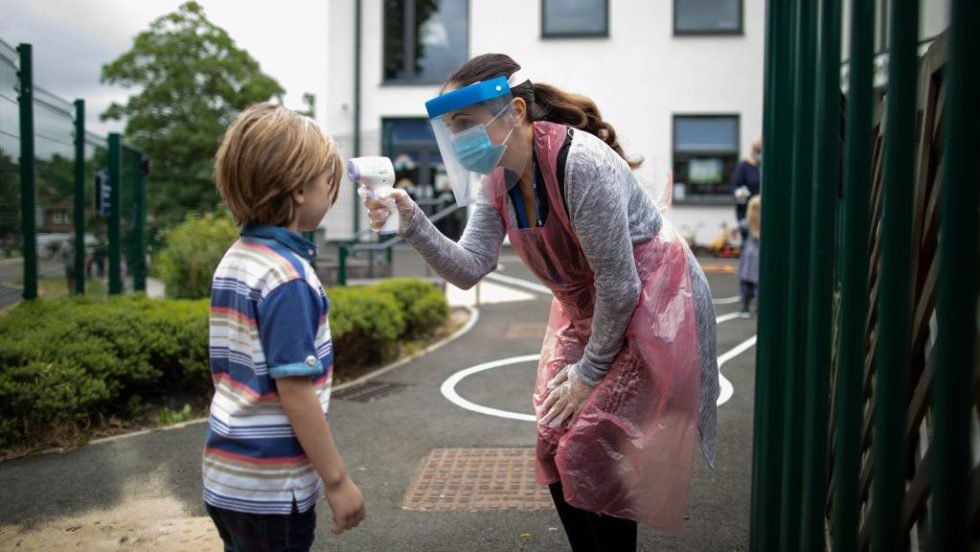 Un enfant se fait prendre la température par une dame portant une visière contre la COVID-19