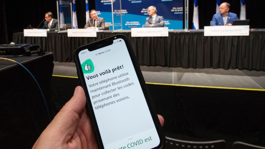 Une main tient un téléphone montrant l'application Alerte COVID pendant le point de presse où François Legault a mis au défi les influenceurs du Québec de télécharger l'application Alerte COVID