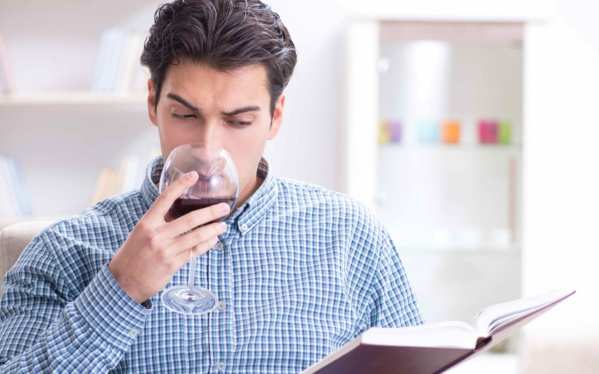 homme qui boit un verre de vin rouge en lisant un livre