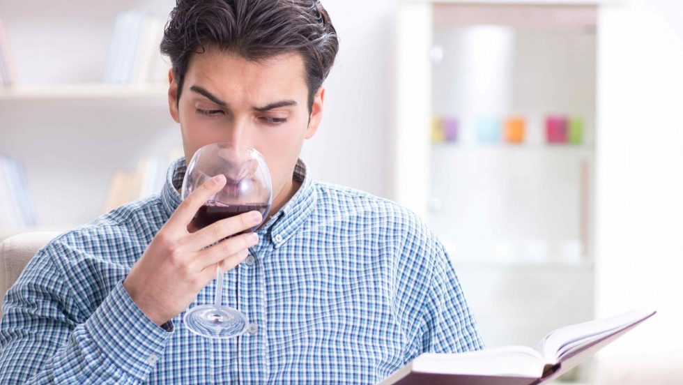 homme qui boit un verre de vin rouge en lisant un livre