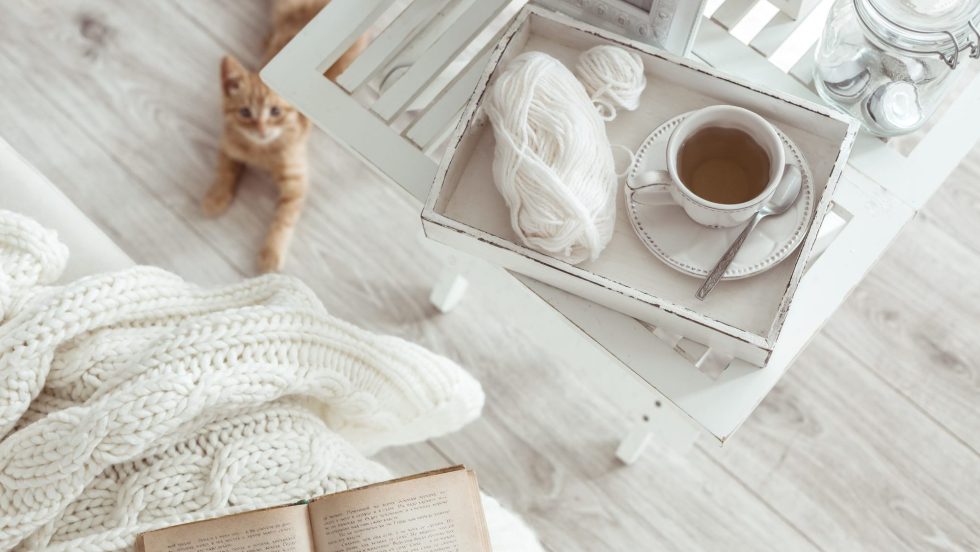 Still life details, cup of tea on retro vintage wooden tray on a coffee table in living room, top view point. Lazy winter weekend with a book on the sofa.