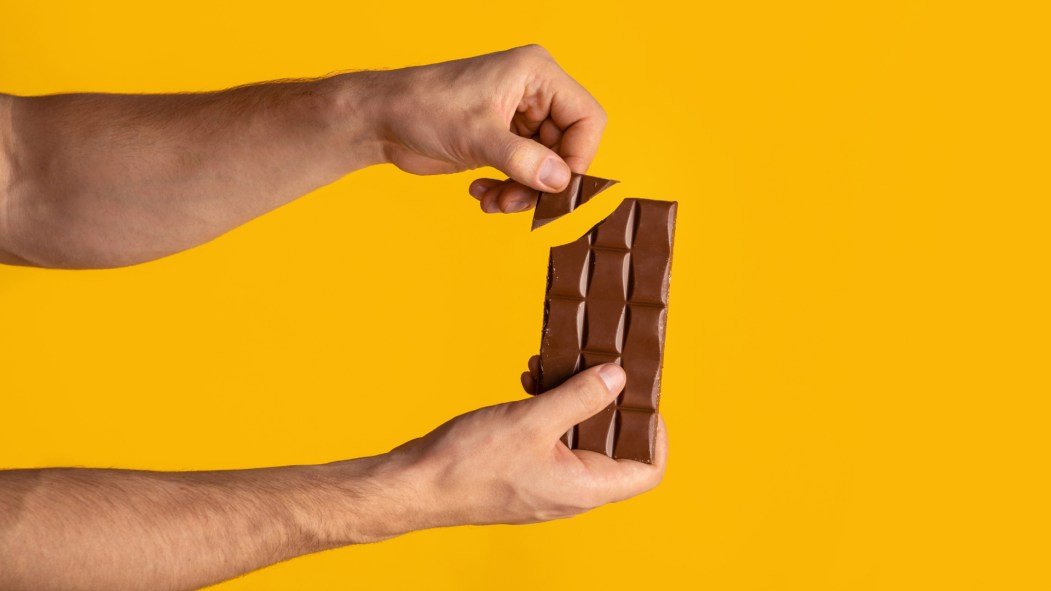 Mains d'homme brisant un carré de chocolat sur une palette entière
