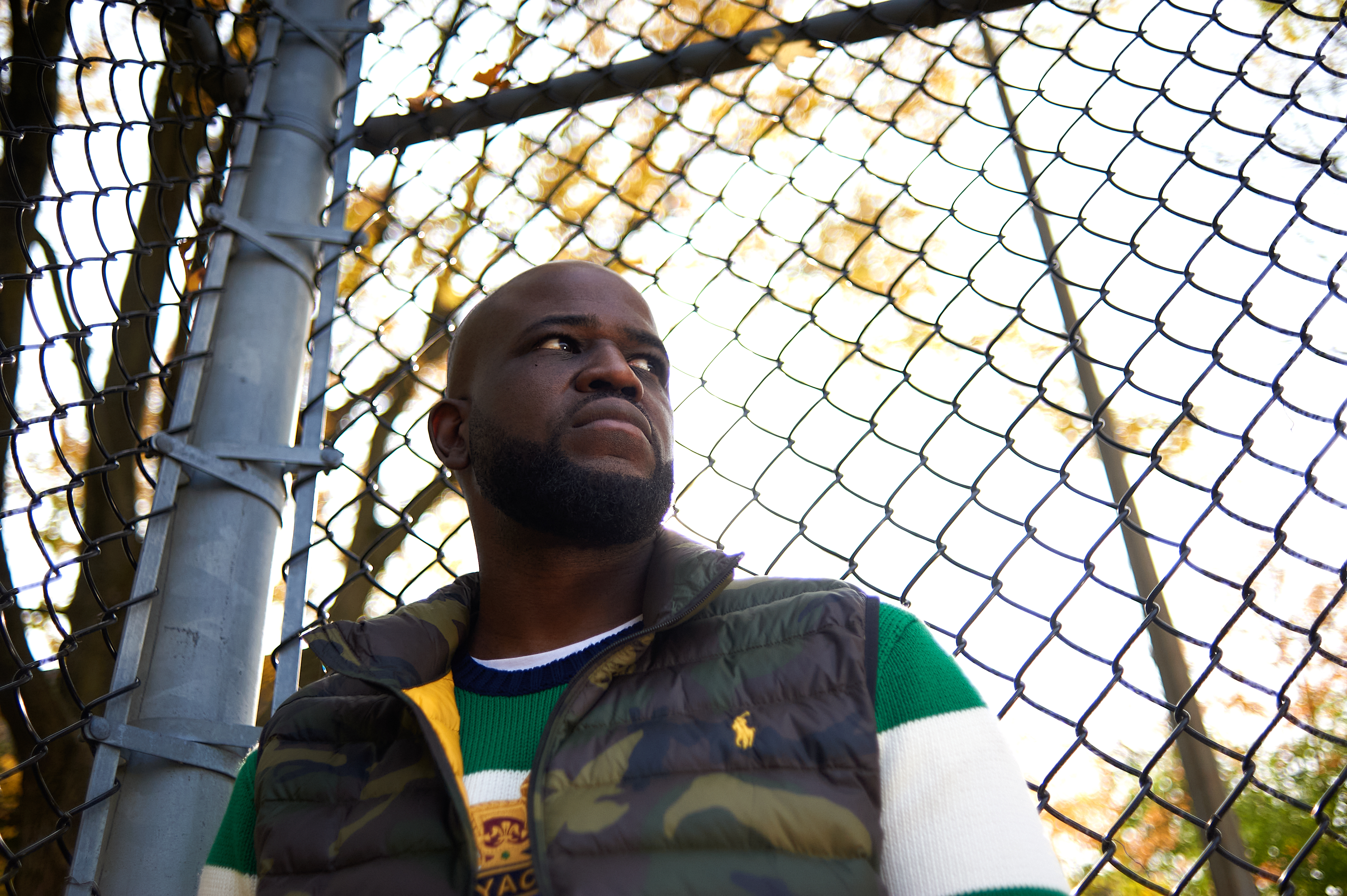 Le rappeur Connaisseur Ticaso pose devant une clôture.