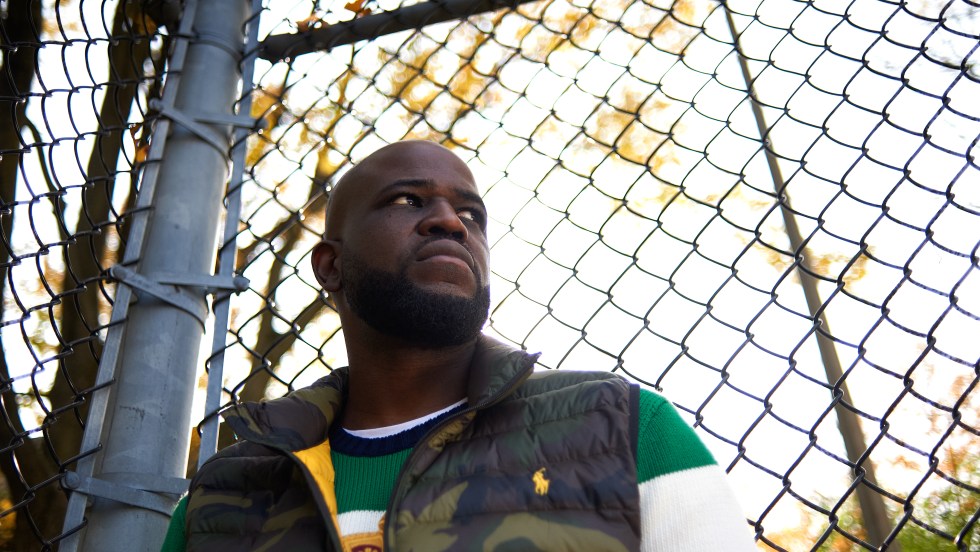 Le rappeur Connaisseur Ticaso pose devant une clôture.