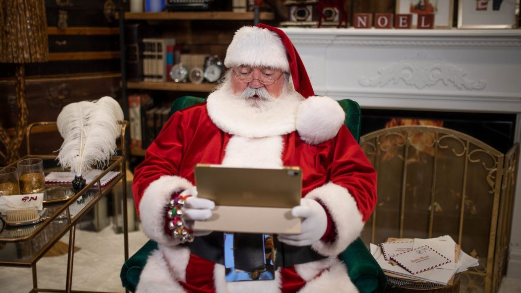 Le père Noël tenant une tablette électronique dans son salon au Pôle-Nord.