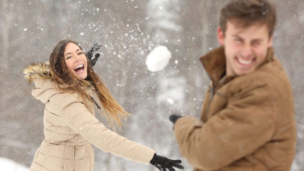 Couple jouant avec de la neige et de la petite amie de lancer une balle en vacances d'hiver