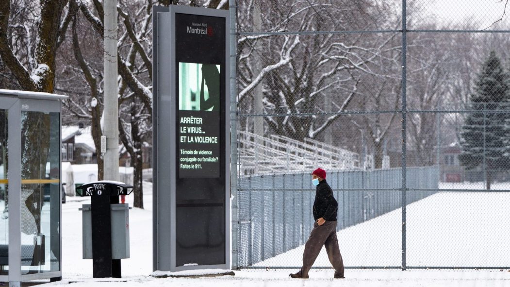 Un homme portant un masque marche dans Montréal-Nord sous la neige.