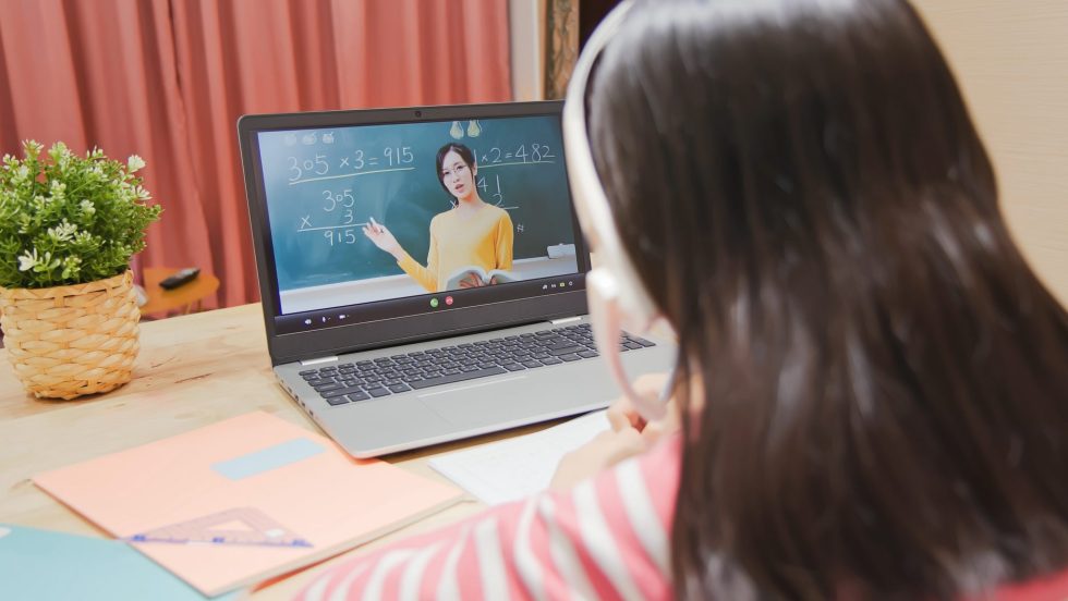 Une petite fille de dos en train de suivre un cours en ligne.