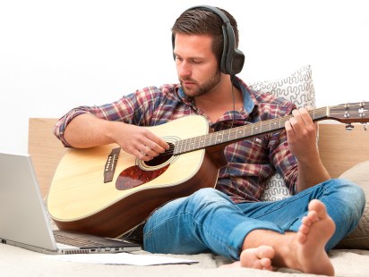Man on sofa playing the guitar with laptop at home