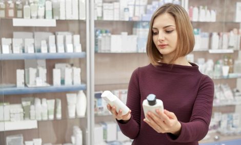 Pharmacy customer standing in drugstore and choosing medical products. Woman looking at cosmetic white bottles. Consumer buying treatment for health care.