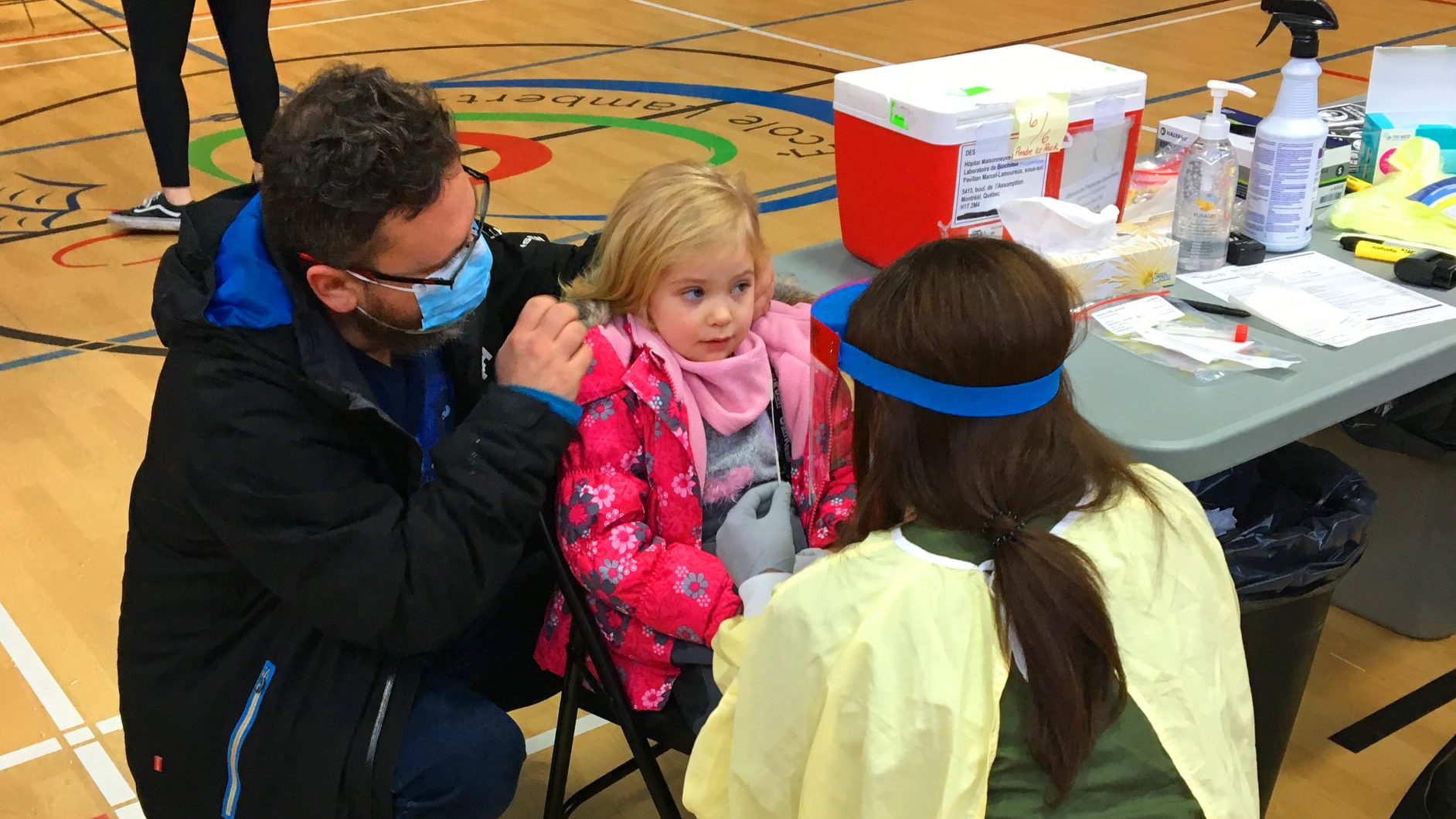 Une petite fille en attente de se faire dépister avec son père et une dépisteuse de dos.
