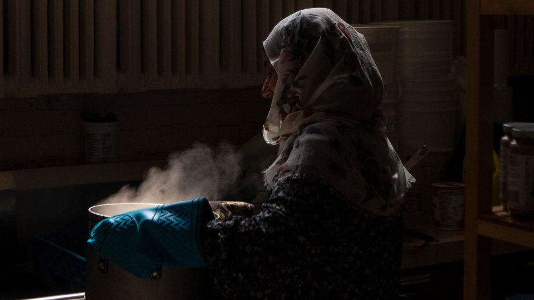 Une femme voilée tenant une casserole fumante à laide de gant en caoutchouc