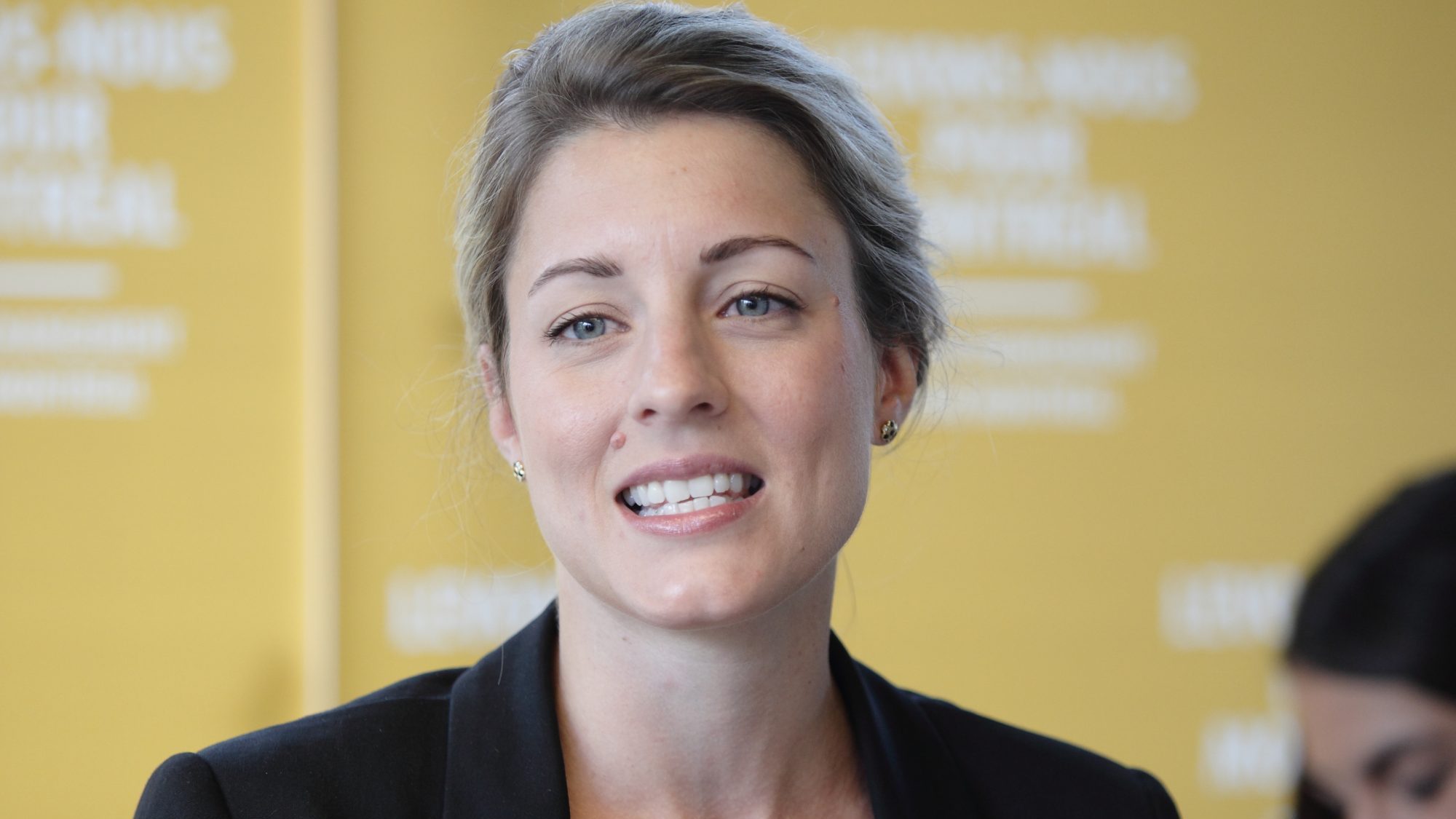 Mélanie Joly devant une affiche jaune du parti Vrai changement pour Montréal