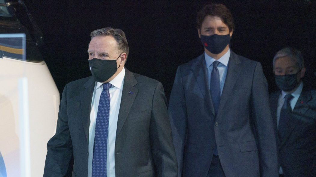 François Legault et Justin Trudeau marchent devant un fond noir, portant des masques
