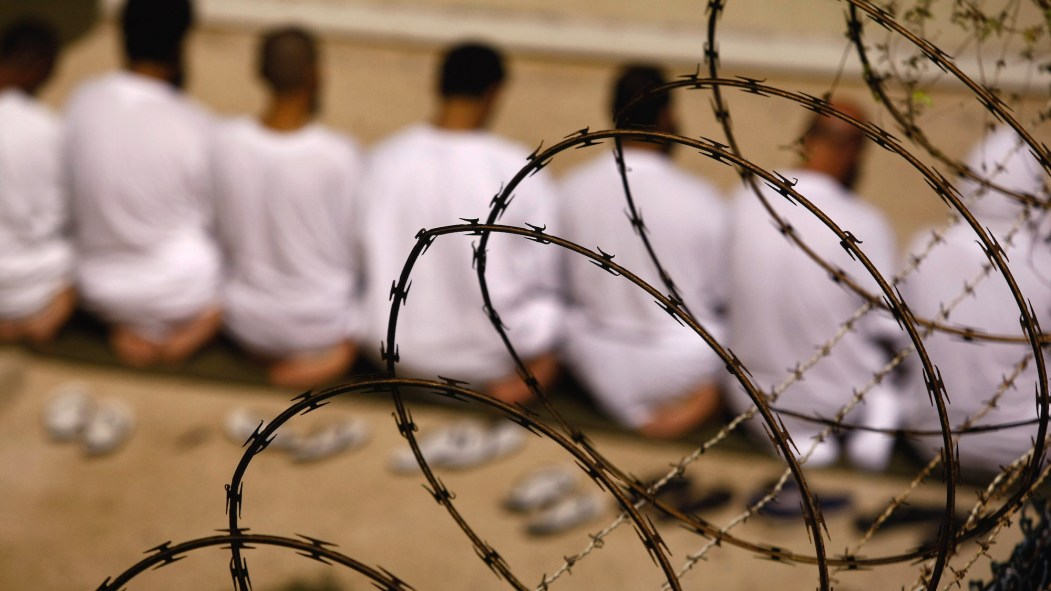 Des prisonniers de la prison de Guantanamo Bay, vus de dos, derrière un barbelé.
