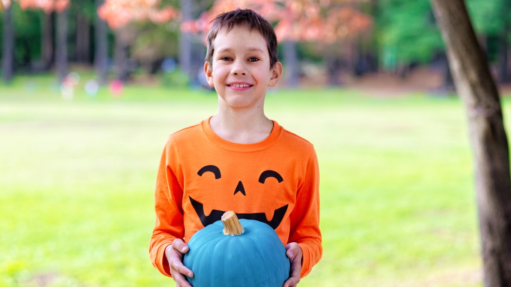 Un jeune garçon tient une citrouille turquoise.