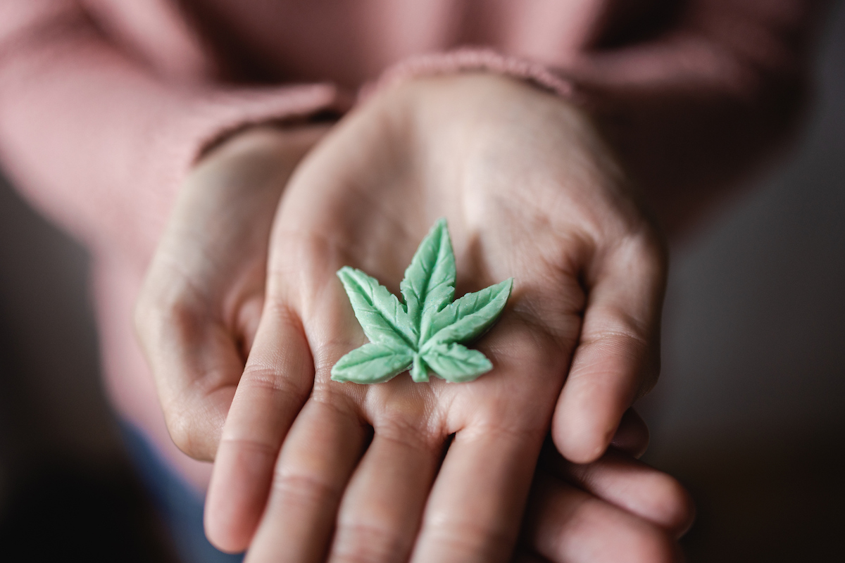 Vue rapprochée de deux mains d'une personne jeune tenant une feuille de cannabis