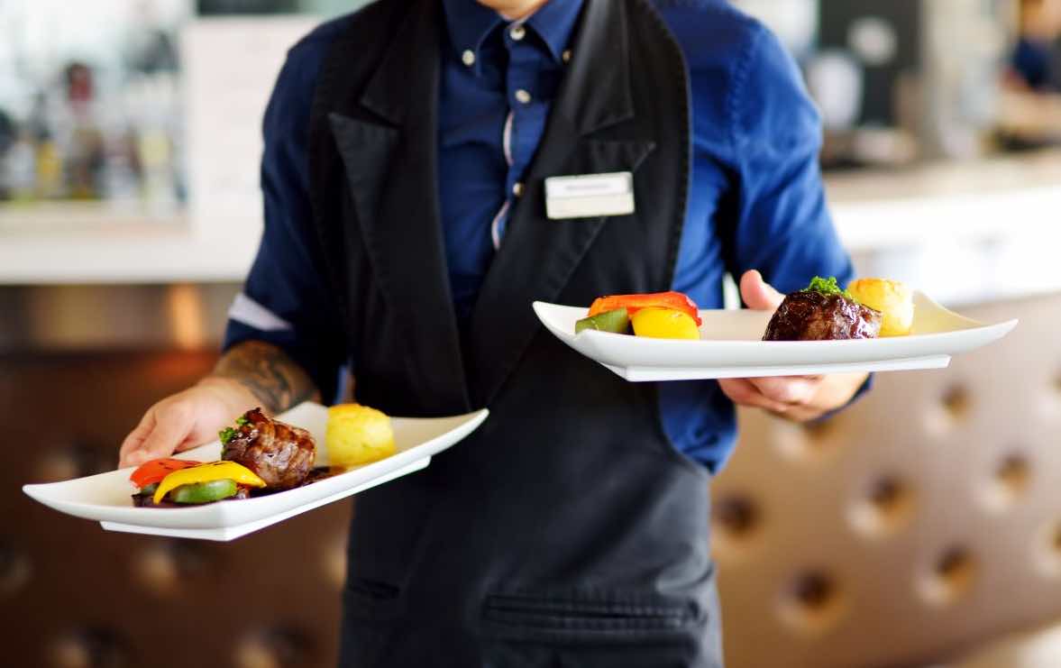serveur au restaurant avec deux plats dans chaque main