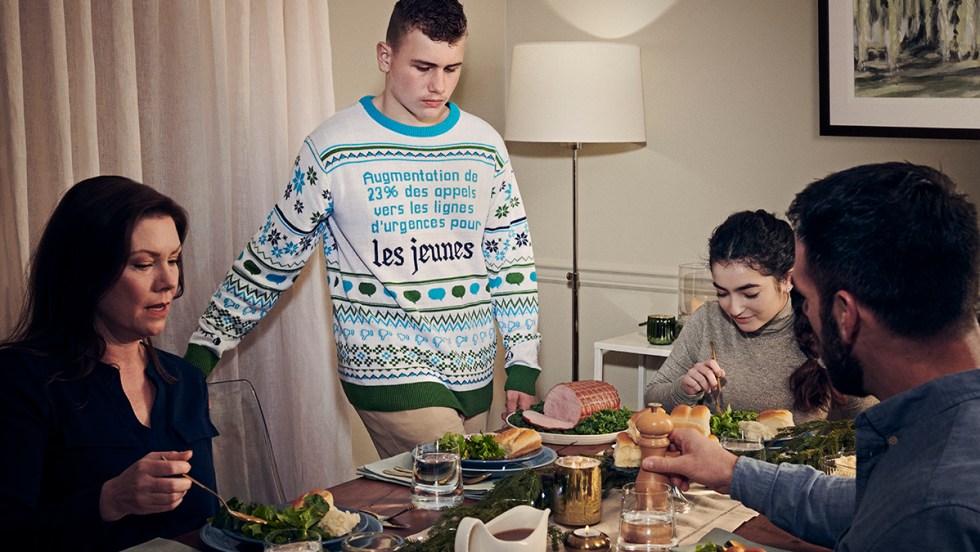 Un jeune homme porte un chandail à manches longues bleu et blanc mentionnant «« augmentation de 23 % des appels vers les lignes d’urgences pour les jeunes ». Il s'agit de la dernière campagne publicitaire de l'Association canadienne pour la santé mentale.