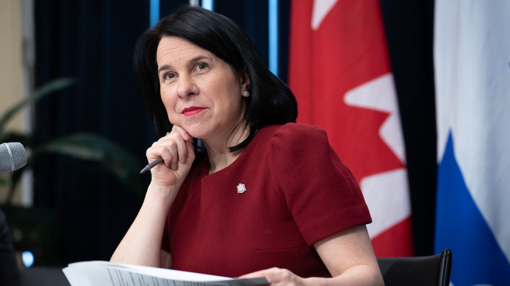 Valérie Plante, mairesse de Montréal, assise à un bureau devant les drapeaux du Canada et du Québec, lors de la présentation de la certification pour propriétaires de logements et du registre des loyers.