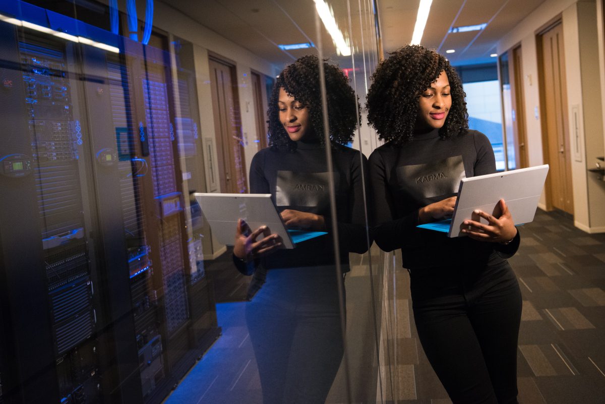 Une femme d'affaires noire consulte son ordinateur dans un corridor.